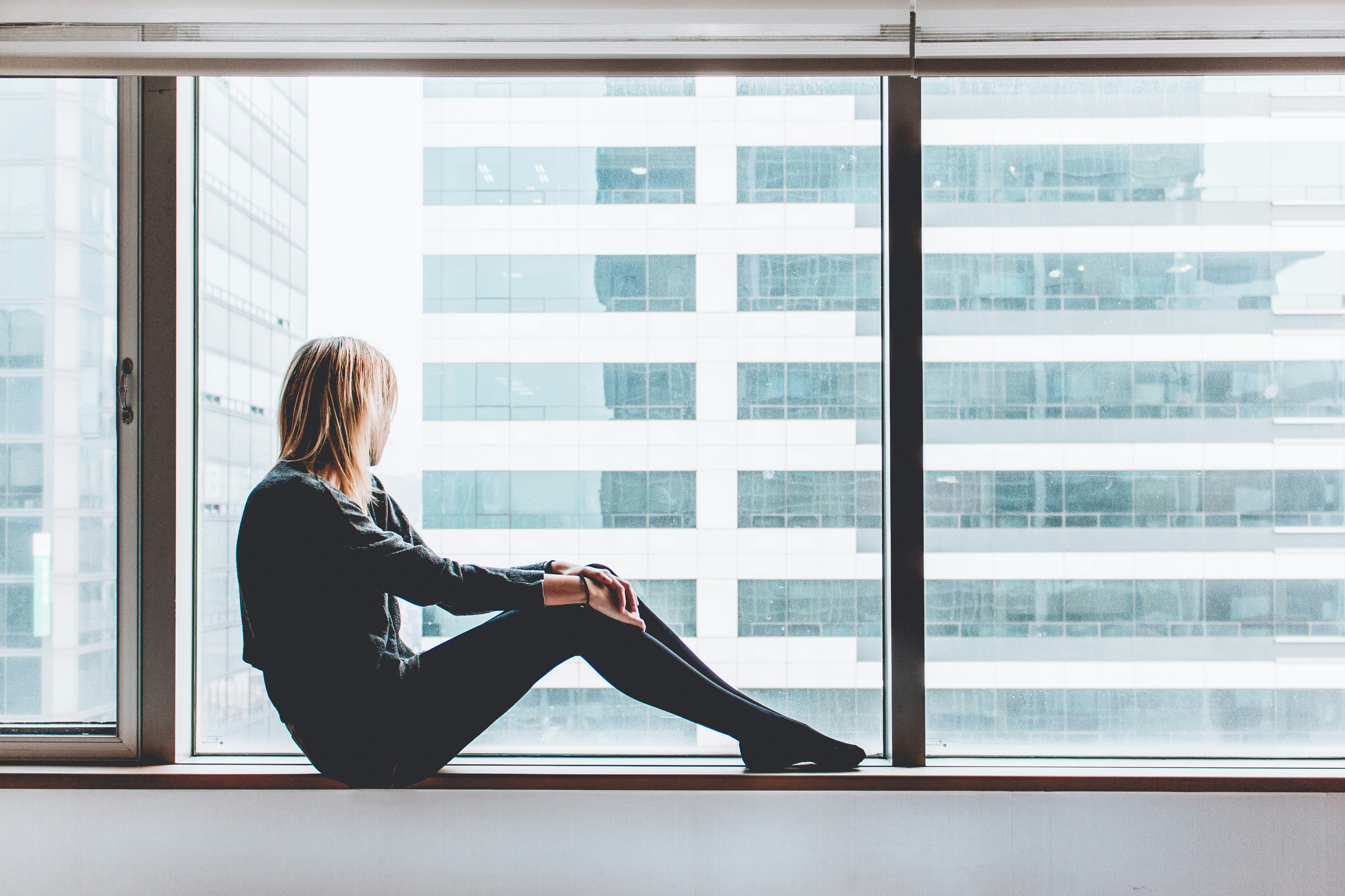 A young blonde woman sitting on a windowsill and looking out the window in Seoul