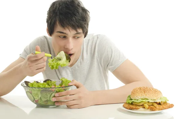 Человек, предлагая вам салат и гамбургер. молодой человек, держа в миску с салатом и большой бургер. Выбор между хорошей здоровой пищи и плохо нездоровой пищи — стоковое фото
